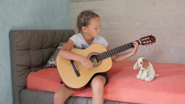 Little girl playing guitar and singing on the sofa in the room