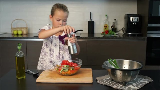 Little girl filling the  salad with oil and pepper in the kitchen