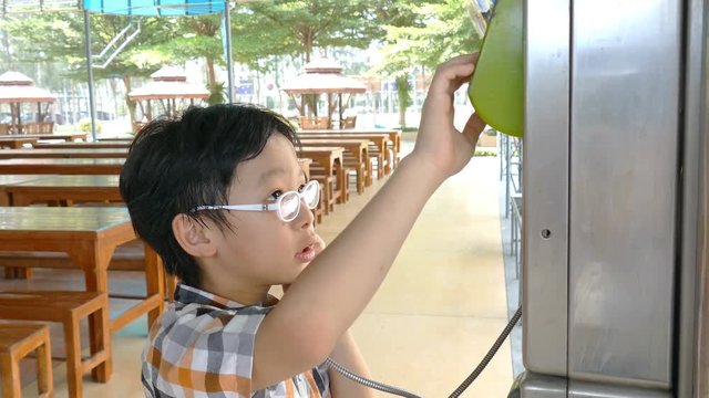 Young asian boy using public phone at school
