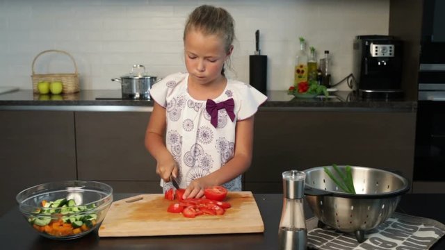Little girl slicing tomatoes for the salad in the kitchen