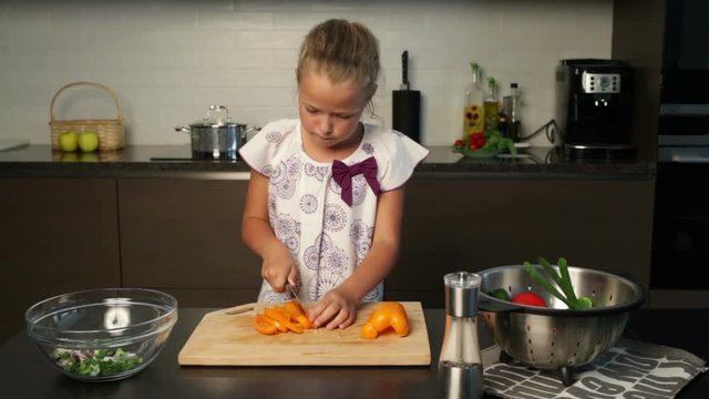 Little girl slicing yellow bell pepper for the salad in the kitchen