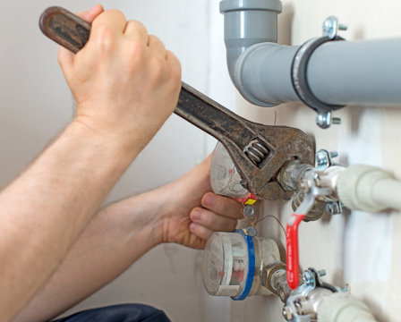 Male plumber fixing water meter with adjustable wrench.