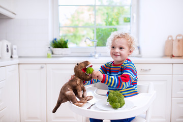 Little boy feeding broccoli to toy dinosaur