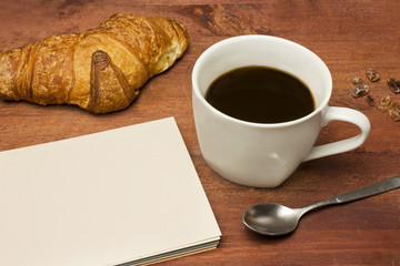 Dark coffee, cane sugar, spoon, croissant, and blank notepad