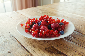 Summer organic berries on plate on wooden table. Agriculture, gardening and harvest concept. Healthy eating and lifestyle