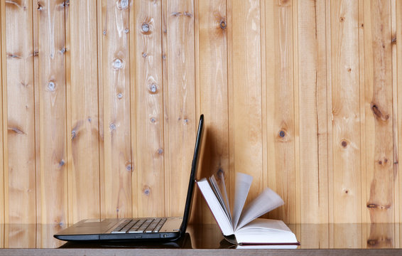 Book and Laptop on a wooden table. Wood background. E-learning.