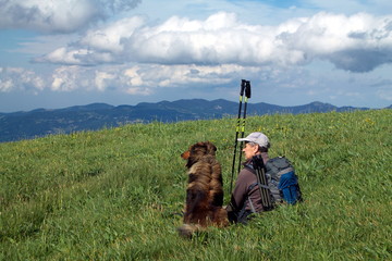 hiker with his dog sitting in the grass watching the view from the top