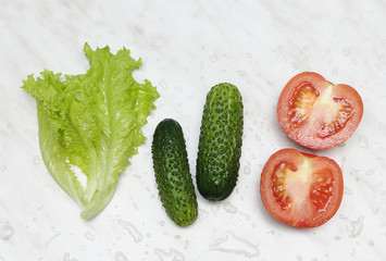 Fresh vegetables - tomato, cucumber and leaf salad - are ready for salad on light marble background 