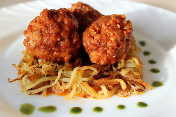 Meatballs in sweet and sour tomato sauce on a crispy crust of potatoes