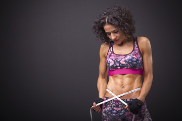 Fit woman with measuring tape on dark background