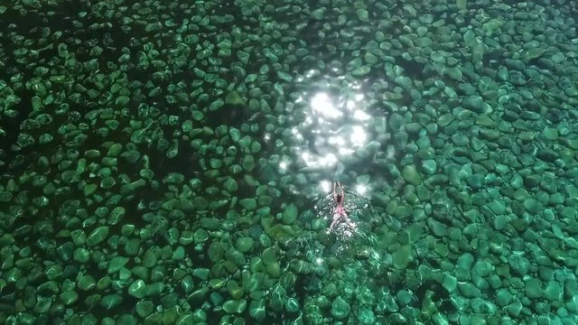 Aerial flight over female swimmer in a pink bikini enjoying swimming in a sea or ocean during her summer vacation