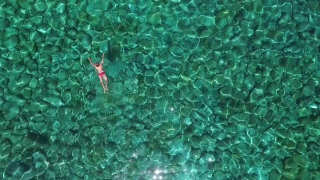 Aerial flight over female swimmer in a pink bikini enjoying swimming in a sea or ocean during her summer vacation
