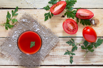 Glass of tomato juice with green leaves on a wooden background,