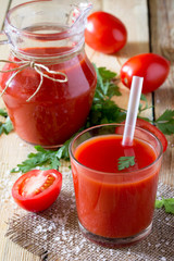Glass of freshly squeezed tomato juice with green leaves on a wo