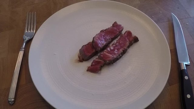 Slow motion salt droping on cutted peaces of red beaf steake with knife and a fog in a video frame
