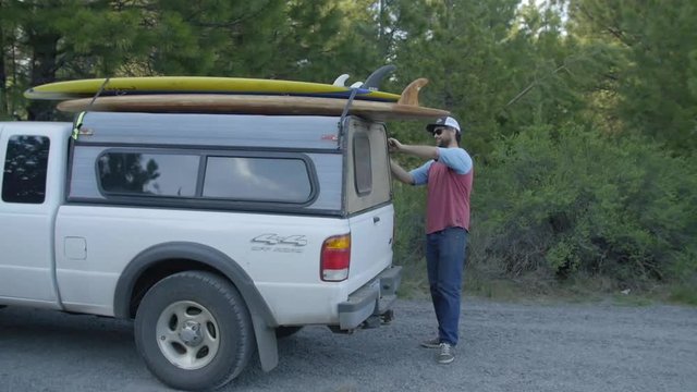 Handsome Bearded Man in sunglasses prepares to get surfboards off his white truck
