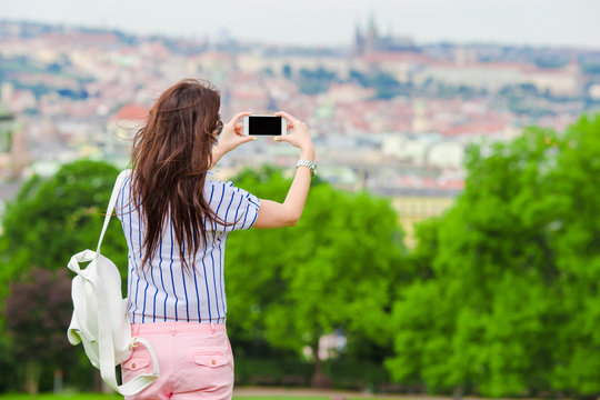 Young caucasian woman making photo of european old city by mobile phone from the observation place