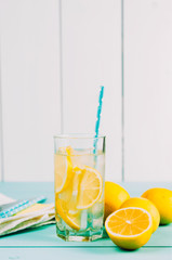 Cold lemonade in a glass with a straw. Fresh lemons on a wooden table.