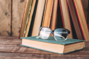 Old books and glasses on wooden brown table.