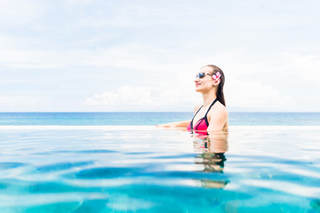Frau in rotem Bikini und Blume im Haar in Infinity-Pool mit Meer im Hintergrund