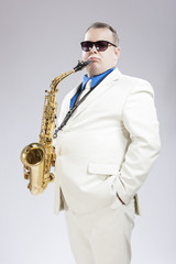 Fototapeta premium Handsome Male Saxo Player in Stylish White Suit and Sunglasses Posing Against White