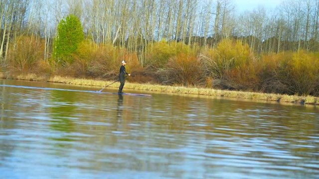 Man in wetsuit glides on river water while on SUP board in slow motion