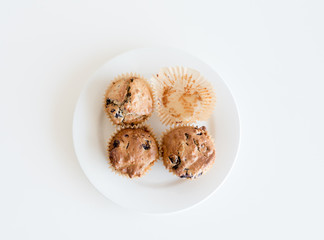 High angle view of three homemade blueberry muffins and an empty muffin case on a white plate on a white table