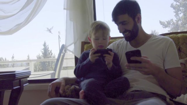 Medium shot of uncle and nephew playing on separate cell phones together 