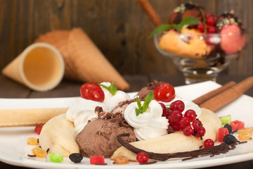 Banana split ice cream with whipped cream,berries and cherry. Ice cream cones in background.