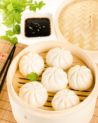 Chinese steamed buns in bamboo steamer basket with cilantro, soy