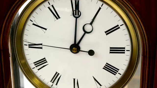 The clock ticks on one oclock it is an old wall clock with a roman numeral numbers on it