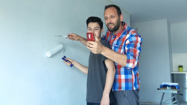 Happy father taking photo of his son during painting their new home, 4K
