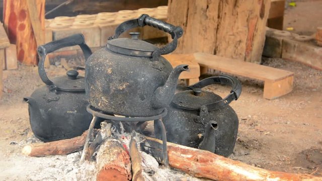 FullHD video - Three blackened, sooty, tea kettles resting over the glowing coals of a smoldering cooking fire.