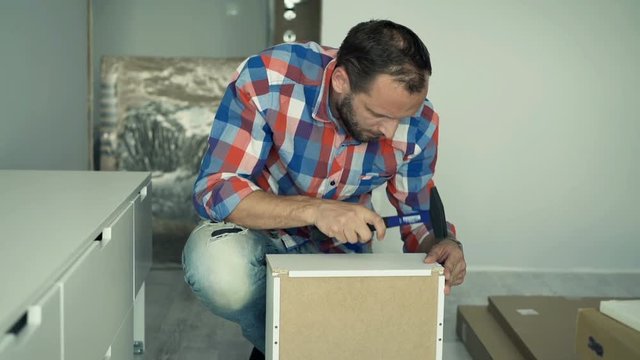 Young man assembling furniture with hammer in his new home, 4K
