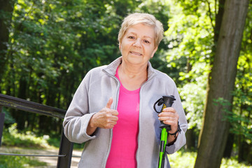 Elderly senior woman holding nordic walking sticks and showing thumbs up
