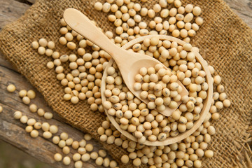 Whole grain soybeans in wooden bowl and spoon on linen sack, rustic and organic crop product concept.