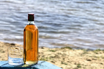 Bottle whiskey and tumbler on shore of lake