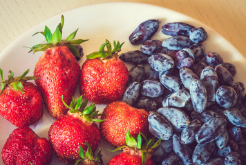 Ripe red strawberry and blue honeysuckle berries on the white pl