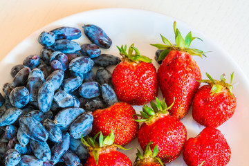 Ripe red strawberry and blue honeysuckle berries on the white pl