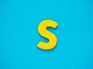 Capital letter S. Yellow letter S from wood on blue background.