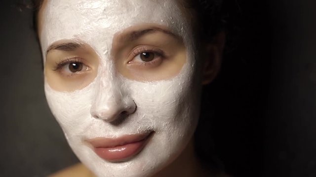 Beautiful young girl with a face pack on her face looking at the camera