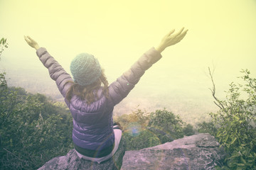 
Woman in violet down jacket with hat raising her arm and turning back in nature