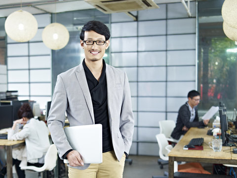 portrait of young asian entrepreneur standing in office smiling