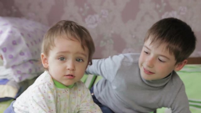 Children lying on the couch in the bedroom watching and smiling at the camera