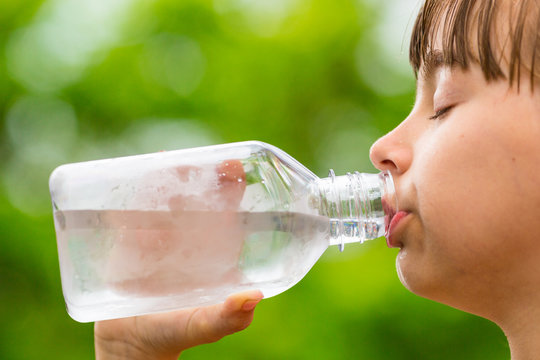 Child drinking clean tap water from transparent plastic bottle