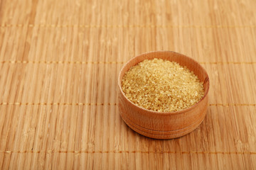Wooden bowl of brown cane sugar on bamboo mat