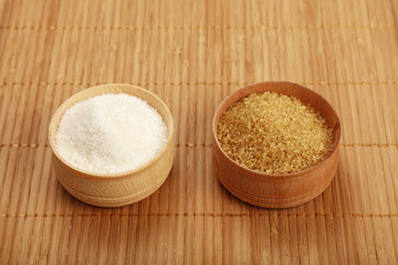 White and brown cane sugar in wooden bowls on mat