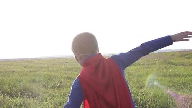 superhero boy running on the green field at sunset