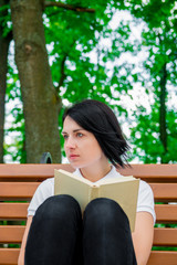 Woman is reading book. Girl with book in white polo, black pant and red shoes is sitting on bench in the park is learning, studying. teenager sitting outdoors with open book