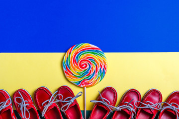 A lot of small red boat shoes near big multi-colored lollipop on colored background.  Top view, copy space. Frame. group of child boat shoes.